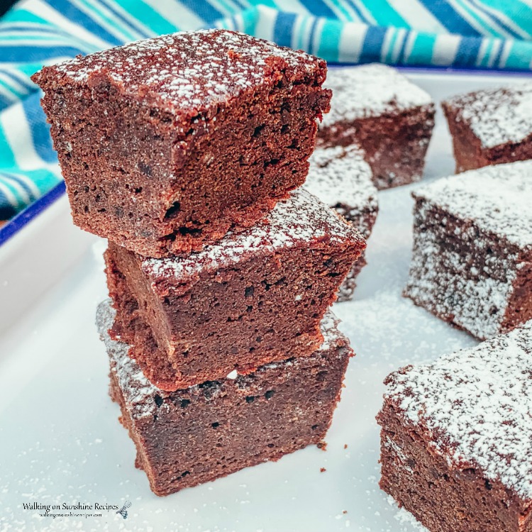 Homemade Brownies with leftover coffee in the batter stacked on white platter with powdered sugar. 