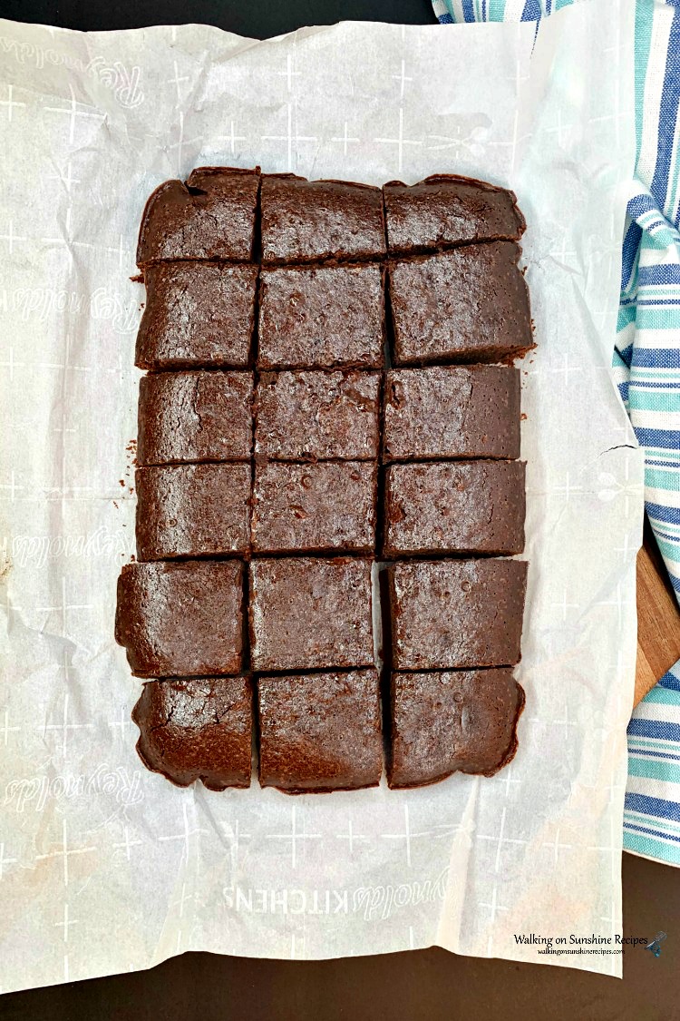 Homemade Brownies made with coffee in the batter sliced with plastic knife on cutting board with parchment paper