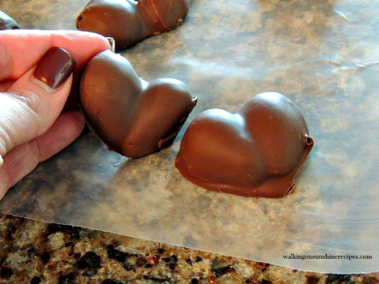Chocolate Covered Heart Shaped Strawberries are the perfect desserts for Valentine's Day or any special occasion you want something sweet and pretty! Heart Shaped Chocolate Covered Strawberries me holding closeup on waxed paper from Walking on Sunshine