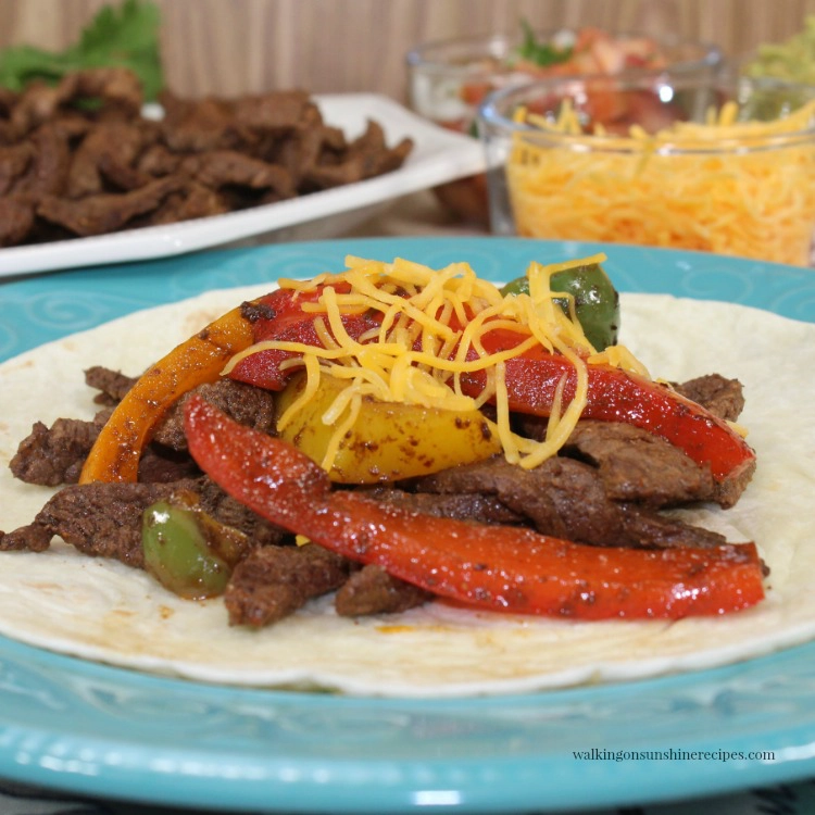 Easy Steak Fajitas on flour tortilla which cheese on top of blue plate. 
