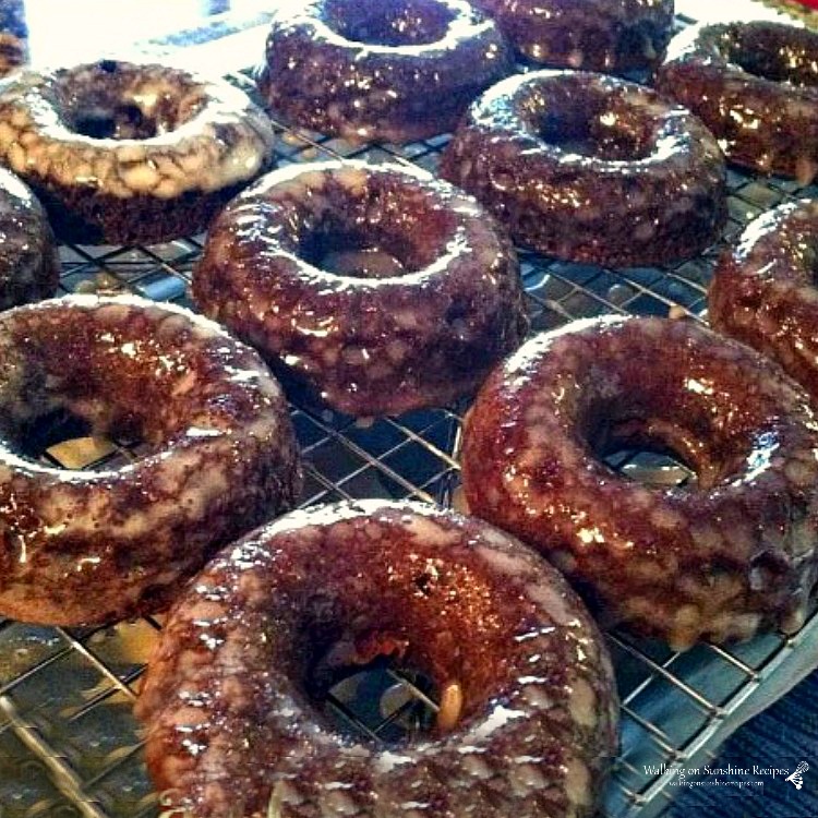 Chocolate Donuts with fresh sugar glaze poured on top sitting on a baking rack. 