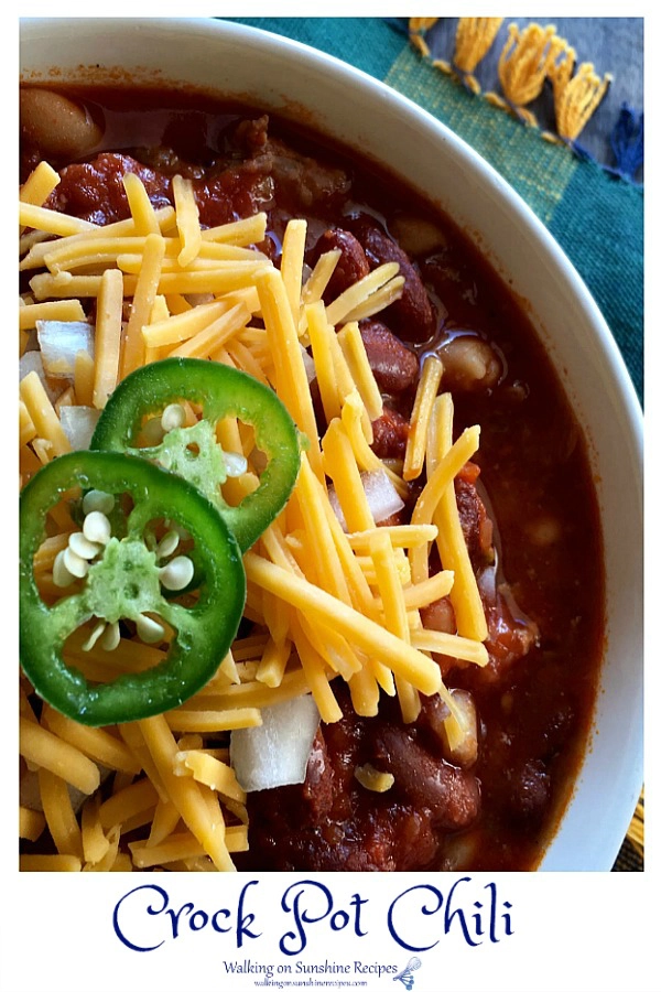 Closeup of ground beef chili with red kidney beans in white bowl with cheddar cheese and jalapenos. 