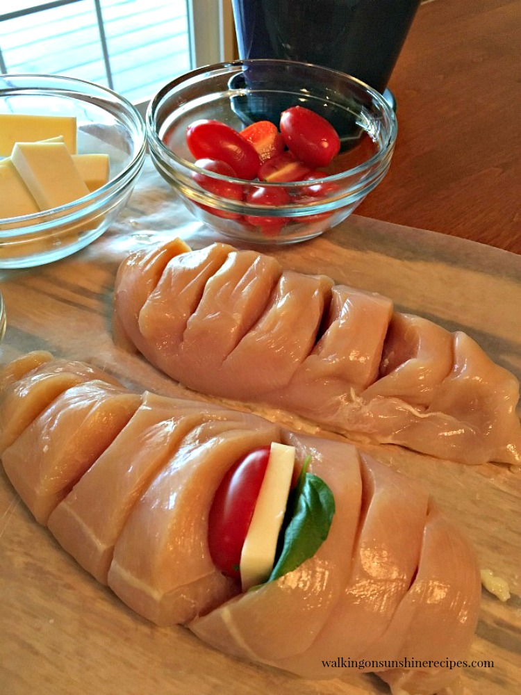 Add sliced mozzarella cheese, grape tomatoes and basil leaves into slits in chicken breast for Hasselback Chicken from Walking on Sunshine Recipes. 