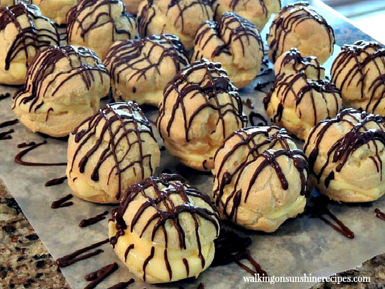 Choux pastry filled with pudding and drizzled with melted chocolate on waxed paper.