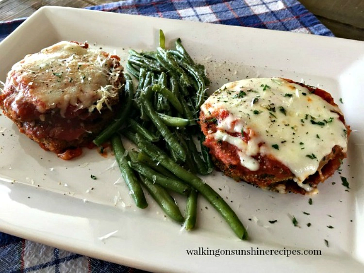 Baked Eggplant Parmesan stacks on white tray with green beans. 