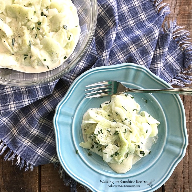 German Cucumber Salad on blue plate on top of blue plaid napkin and wooden board.