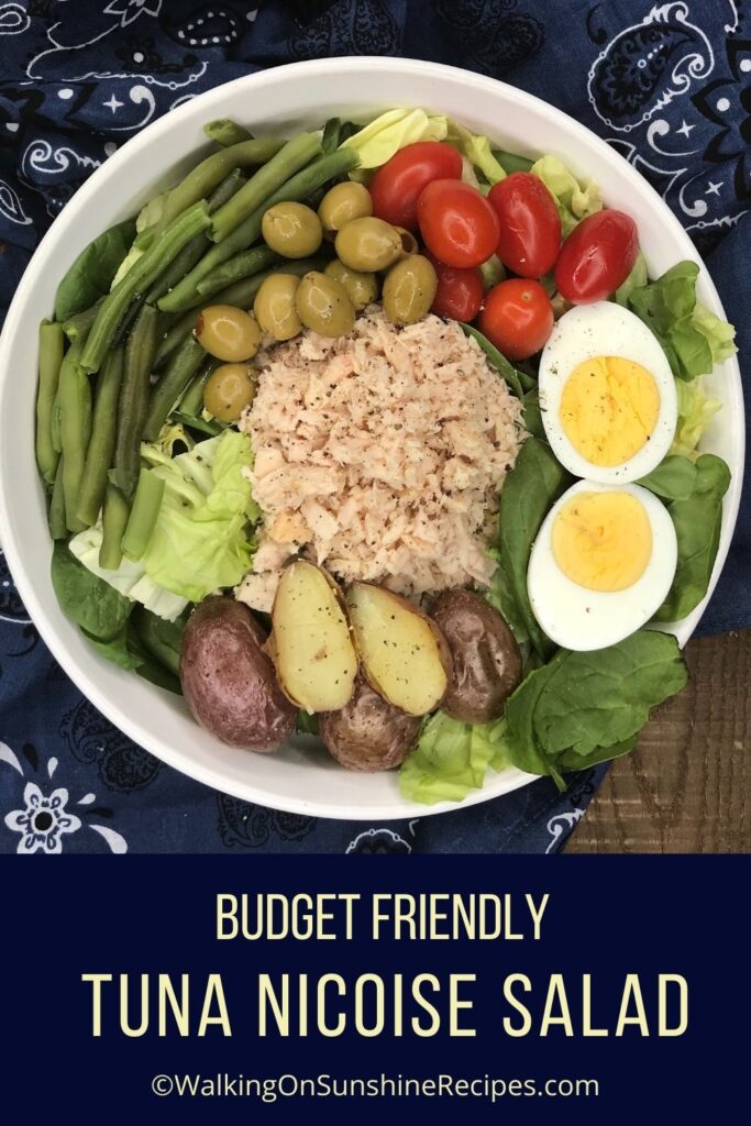 Tuna salad on white plate with eggs, green beans, tomatoes, potatoes and olives.