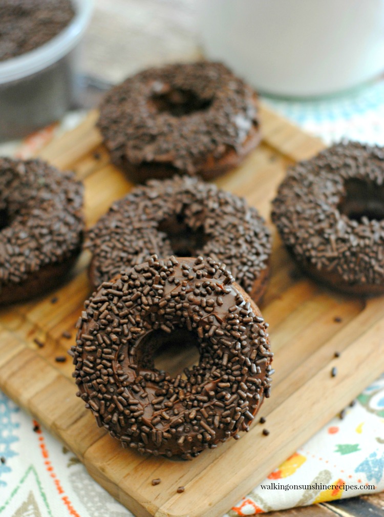 Baked Chocolate Donuts with chocolate frosting and sprinkles on wooden cutting board. 