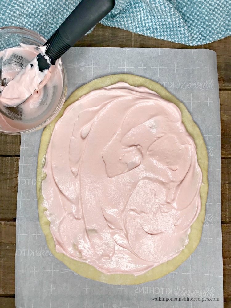 Spread pink cream cheese frosting on top of cooled baked egg shaped pizza crust. 
