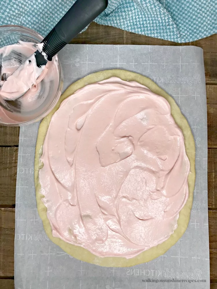 Spread pink cream cheese frosting on top of cooled baked egg shaped pizza crust. 
