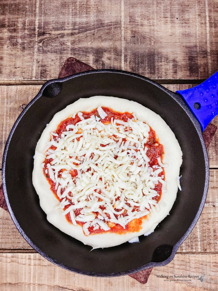 https://walkingonsunshinerecipes.com/wp-content/uploads/2019/06/Add-Cheese-to-the-top-for-cast-iron-pan-pizza.jpg