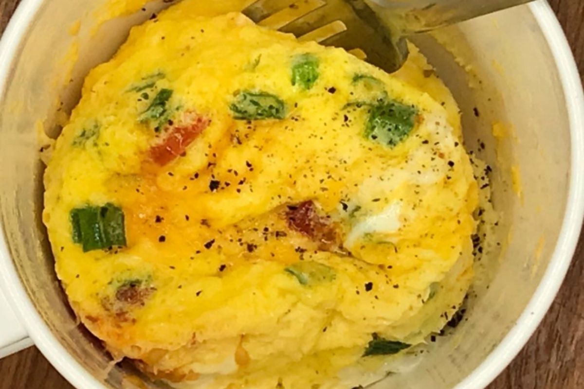 Mug filled with fluffy scrambled eggs and veggies.