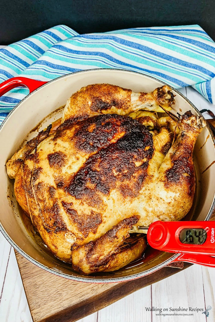 Instant Read Thermometer in thigh of whole roasted chicken in a cast iron dutch oven pan