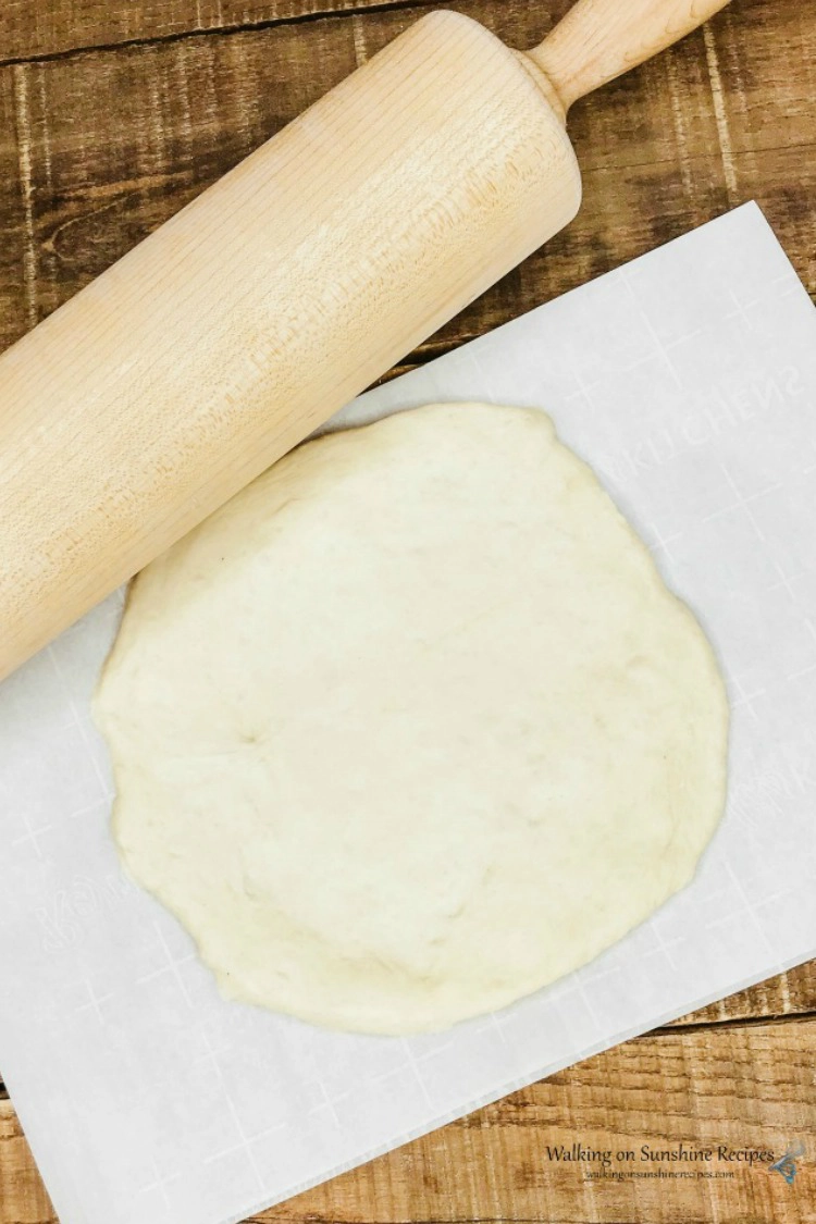 Rolling out Rustic pizza dough with a rolling pin on top of parchment paper. 
