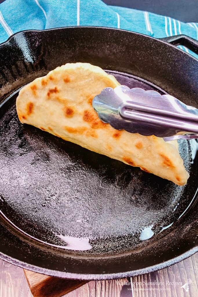 Flatbread baked in cast iron pan being flipped with metal tongs. 