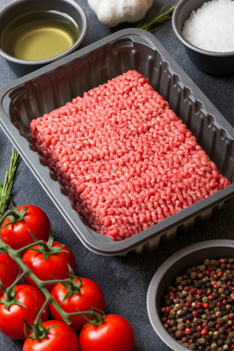 Raw Ground Beef in package with vine tomatoes on cutting board