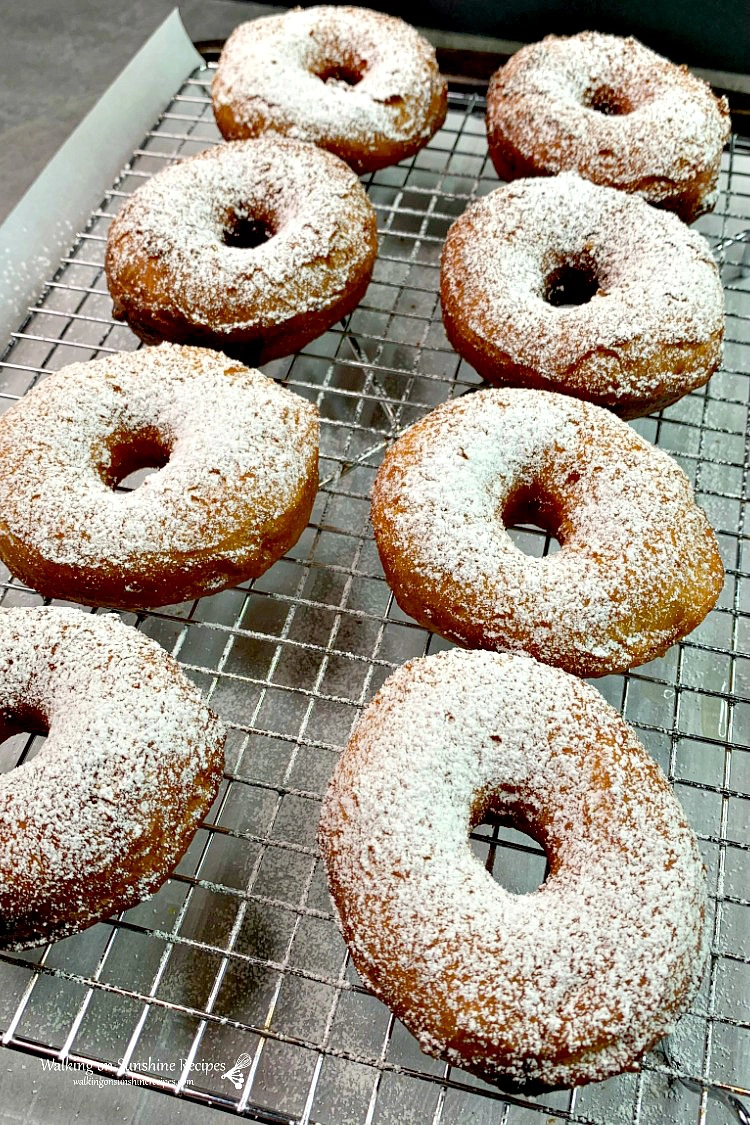 Powdered sugar canned biscuit donuts on baking rack cooling. 