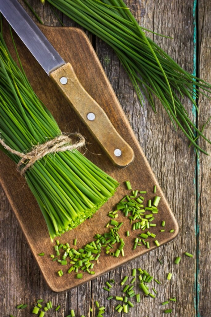 Chopped chives on cutting board with knife. 