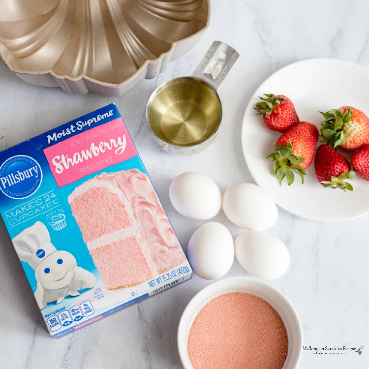 Strawberry Cake Mix box with bundt pan, eggs and fresh strawberries on plate for Cake Mix Baking Secrets. 