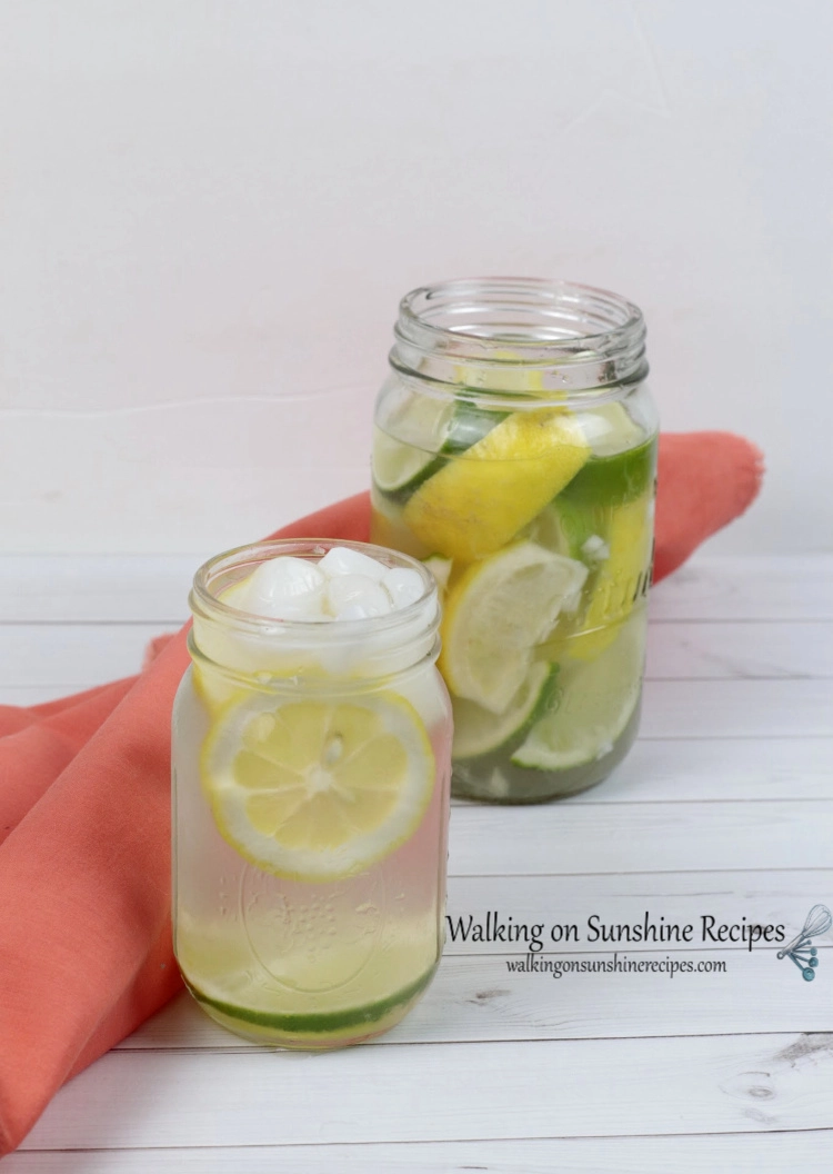 Large and small mason jars containing lemons, limes, water and ice. Displayed besdie an orange cloth napkin. 