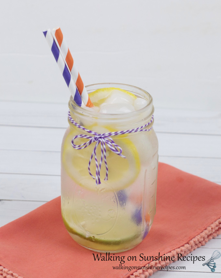 Lemon lime water in a mason jar with purple and orange striped paper straws. Displayed on an orange cloth napkin.