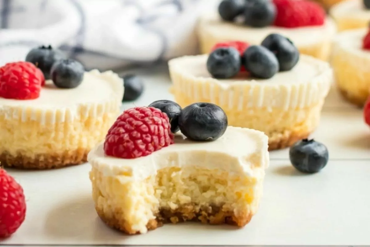 A close-up of mini cheesecakes topped with fresh raspberries and blueberries.