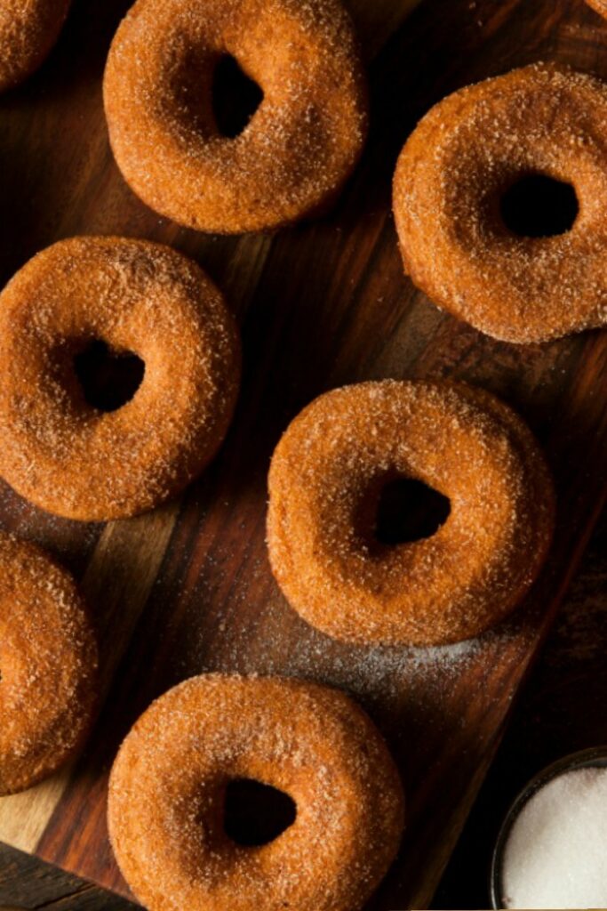 Freshly baked cake mix donuts topped with cinnamon and sugar on cutting board. 