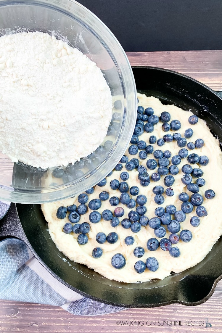 Add  crumb topping to blueberry coffee cake in cast iron skillet pan