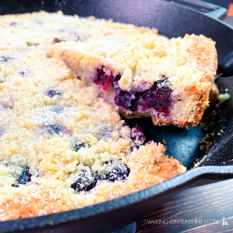 Closeup of a piece of blueberry crumb coffee cake being served from a cast iron skillet pan.