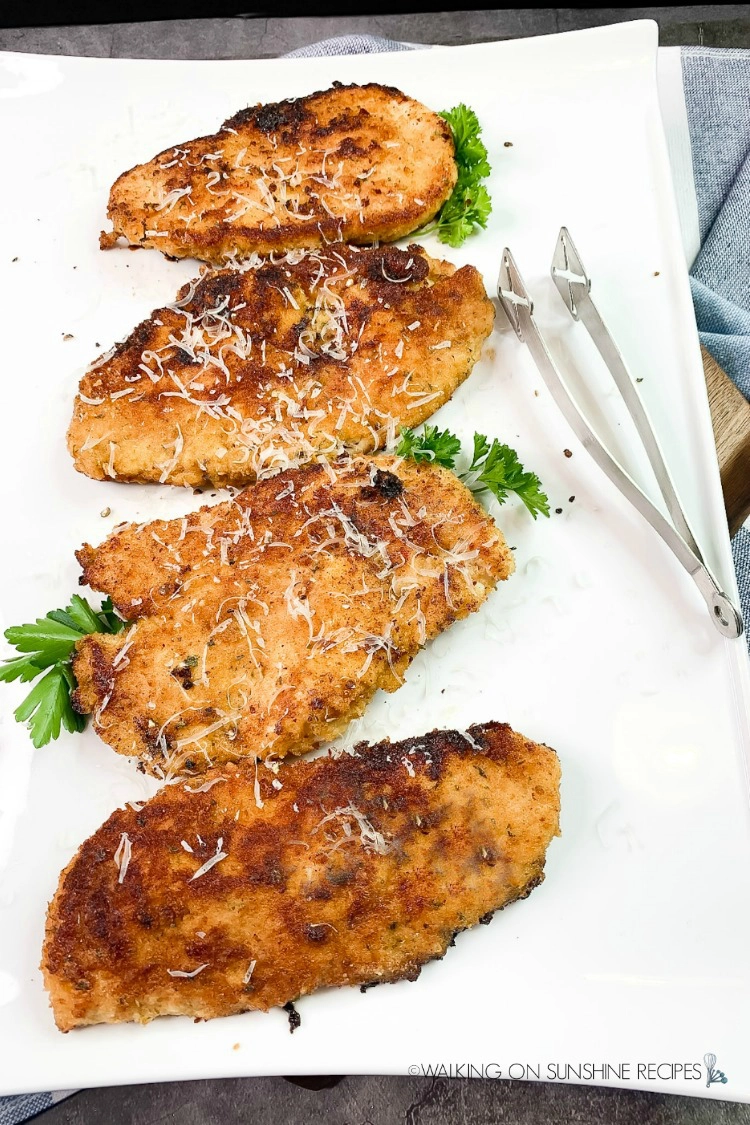 Four boneless skinless chicken breasts cooked on white platter. 