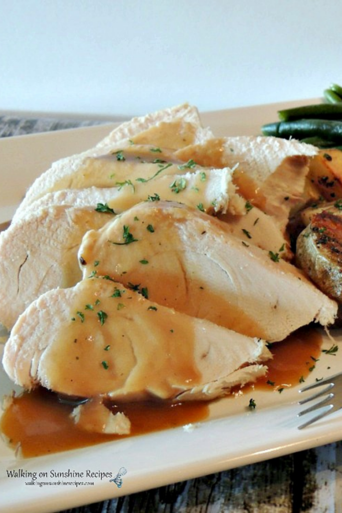Turkey breast with gravy and potatoes on white platter. 
