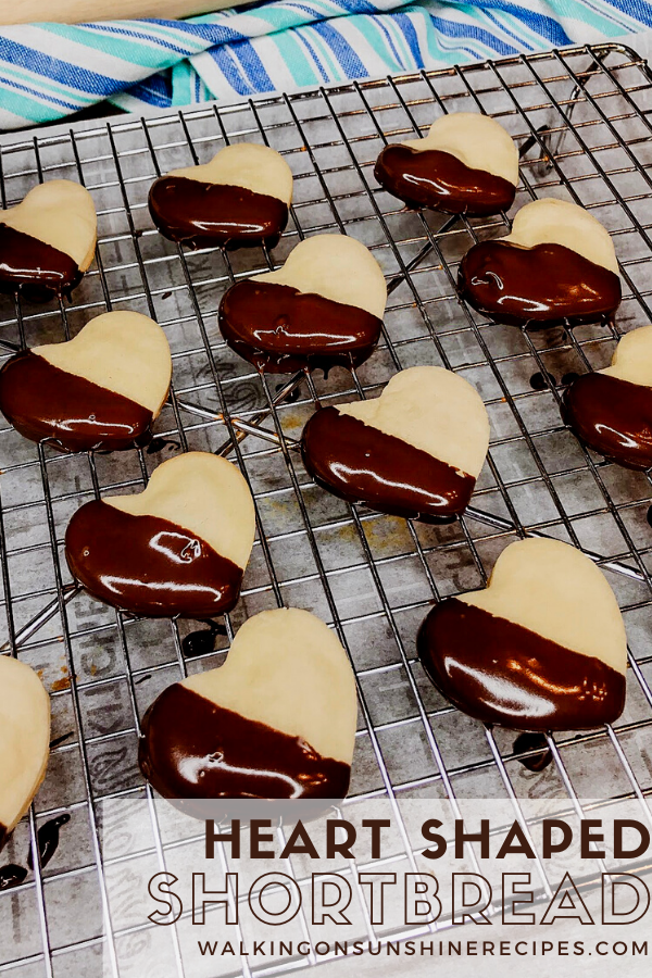 Heart shaped shortbread cookies dipped in melted chocolate on baking rack. 