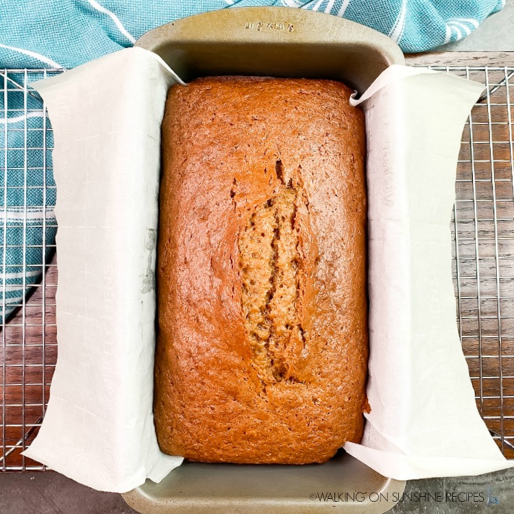 Baked pumpkin bread in loaf pan with parchment paper on baking rack. 