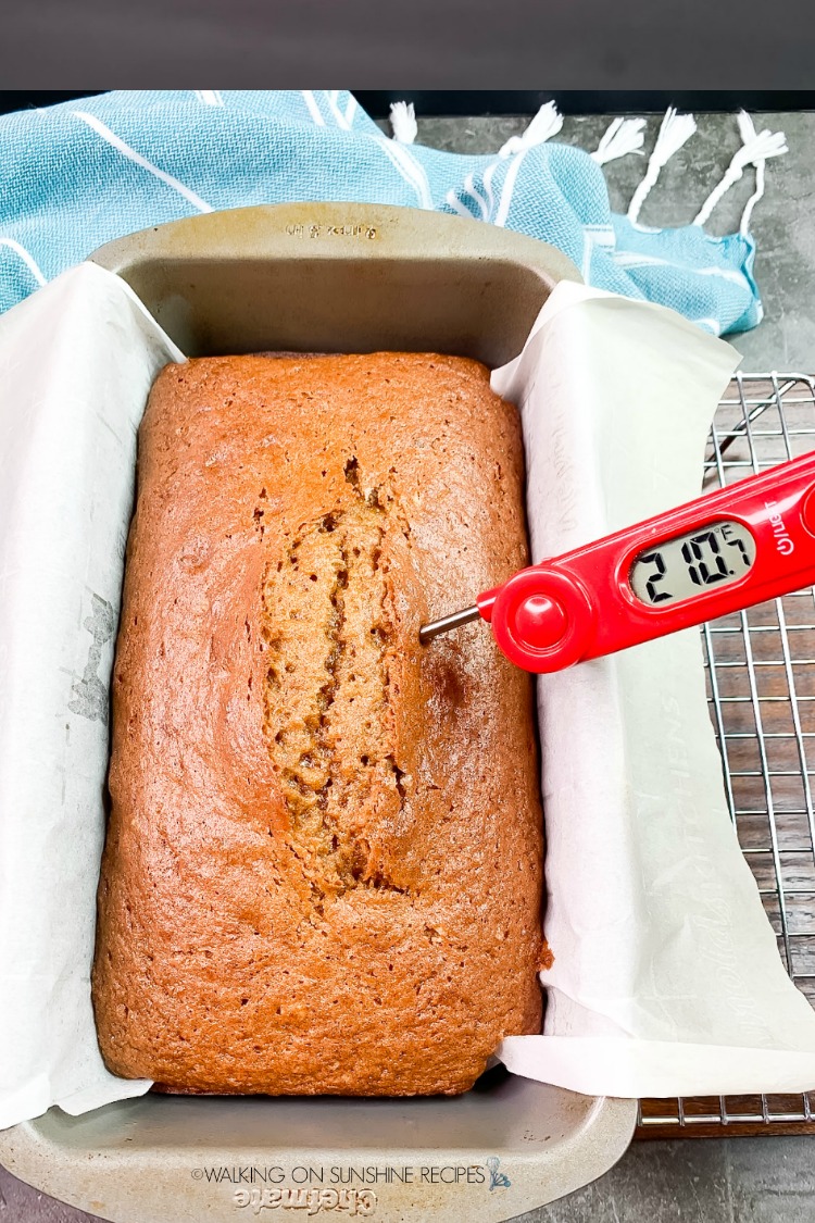 Baked loaf of pumpkin bread with digital thermometer showing internal temperature of cooked bread. 