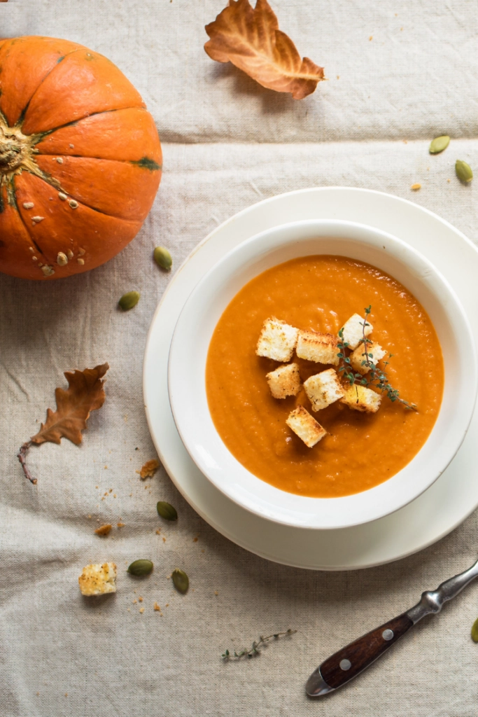 Pumpkin soup in bowl with pumpkin on table. 