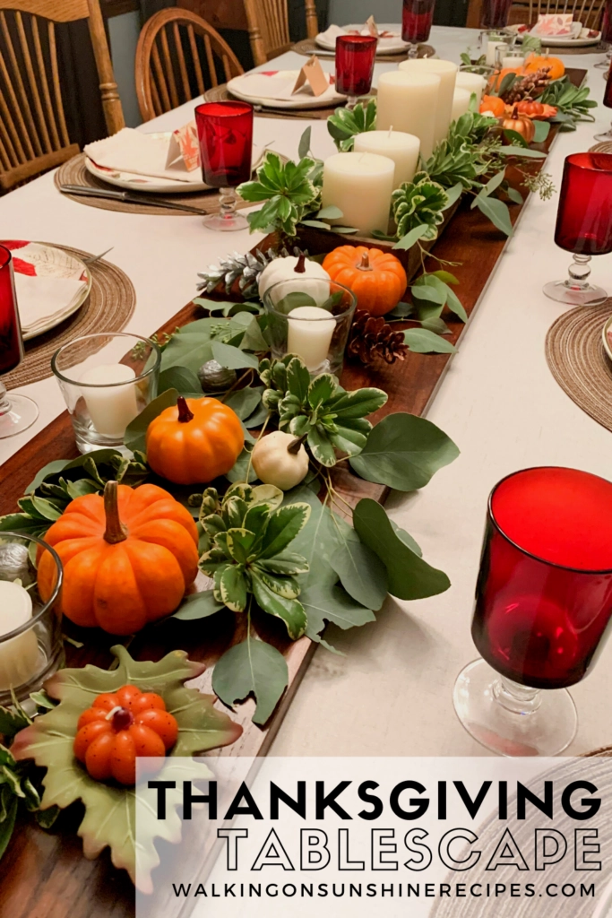 dining room table set with dishes, glasses, candles, pumpkins and greenery. 