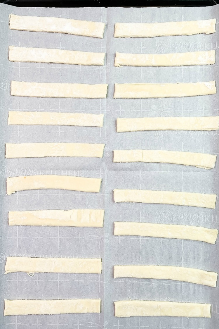 Frozen sheet of puff pastry cut into strips on baking tray. 