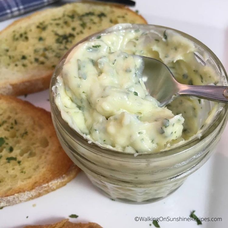 Preceita de manteiga de alho para barrar em pequeno frasco de pedreiro com pão de alho tostado no prato.