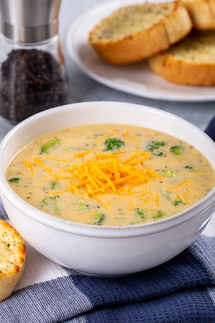 broccoli cheese soup in white bowl with garlic bread on side dish. 