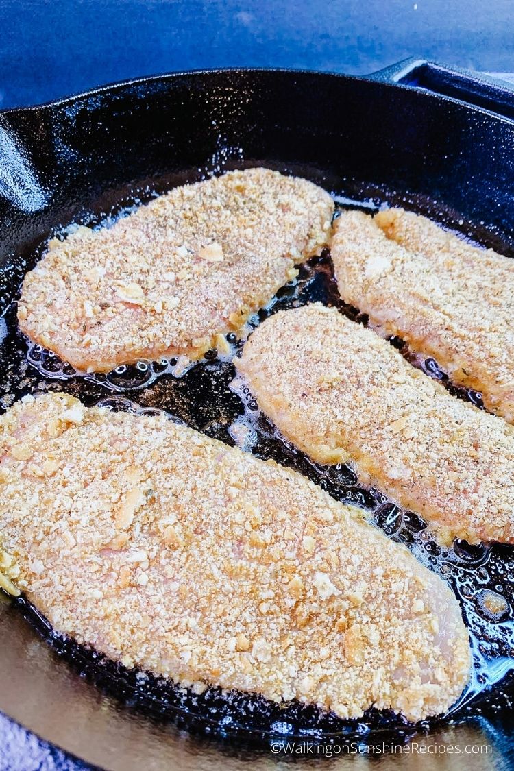 breaded chicken cutlets in cast iron skillet pan. 