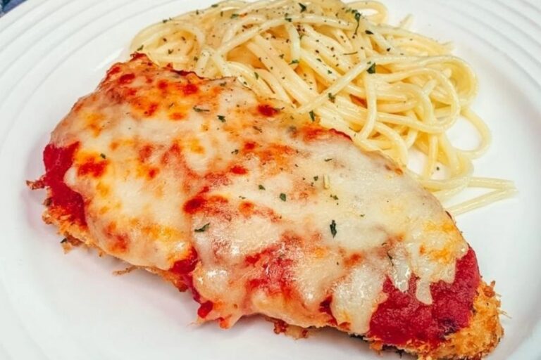 A plate of Chicken Parmesan with a side of spaghetti. The chicken is breaded and topped with marinara sauce and melted cheese.