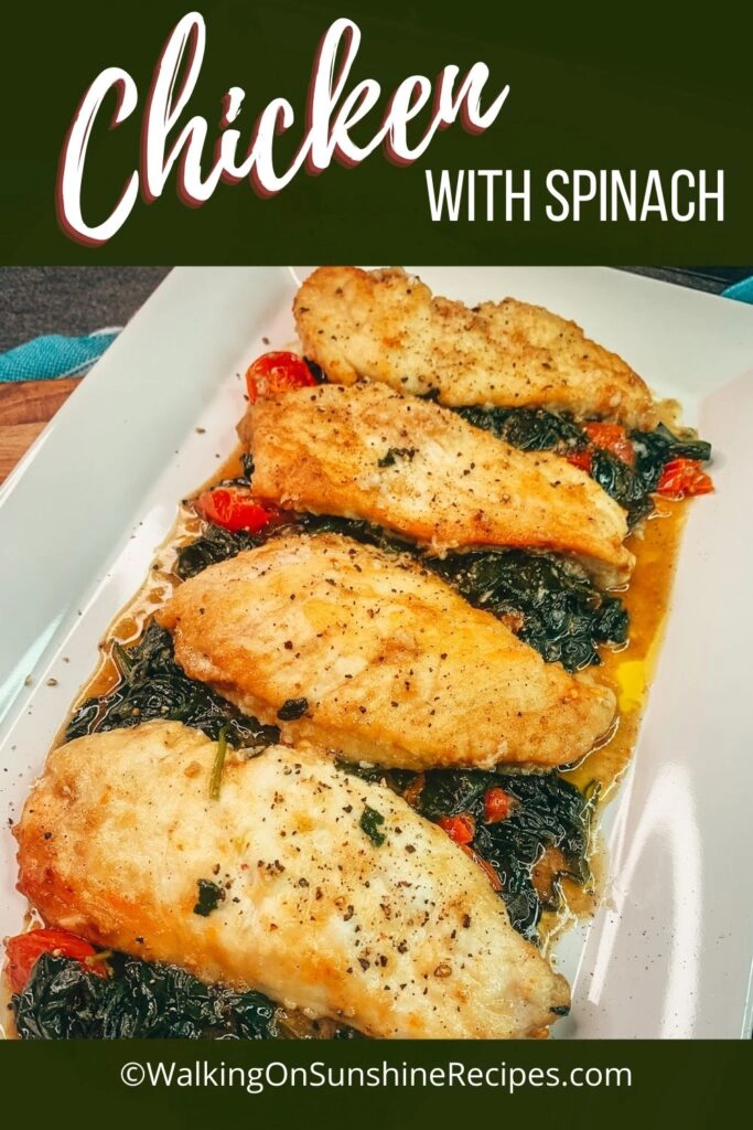 Chicken with spinach and tomatoes on white platter. 