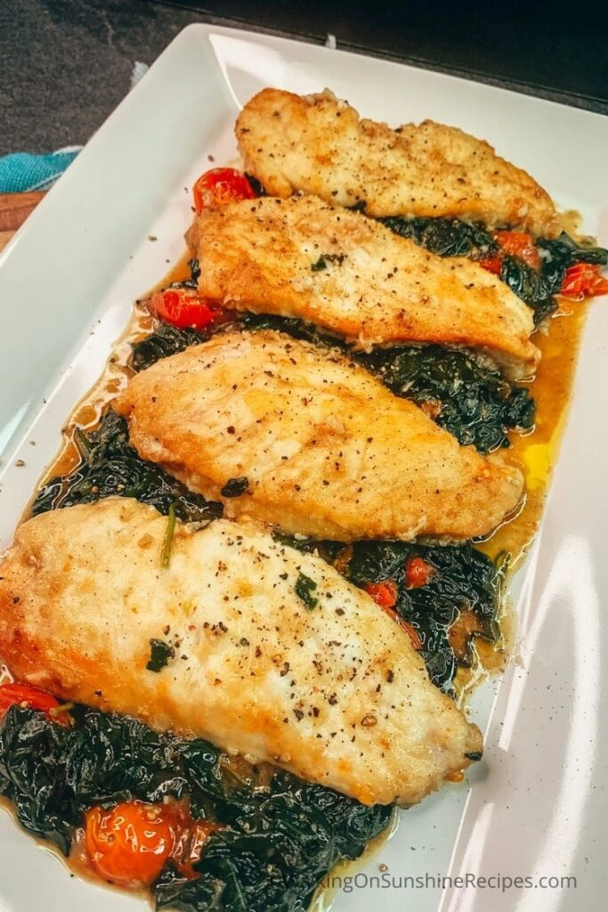 Chicken cooked with spinach and tomatoes on white platter. 