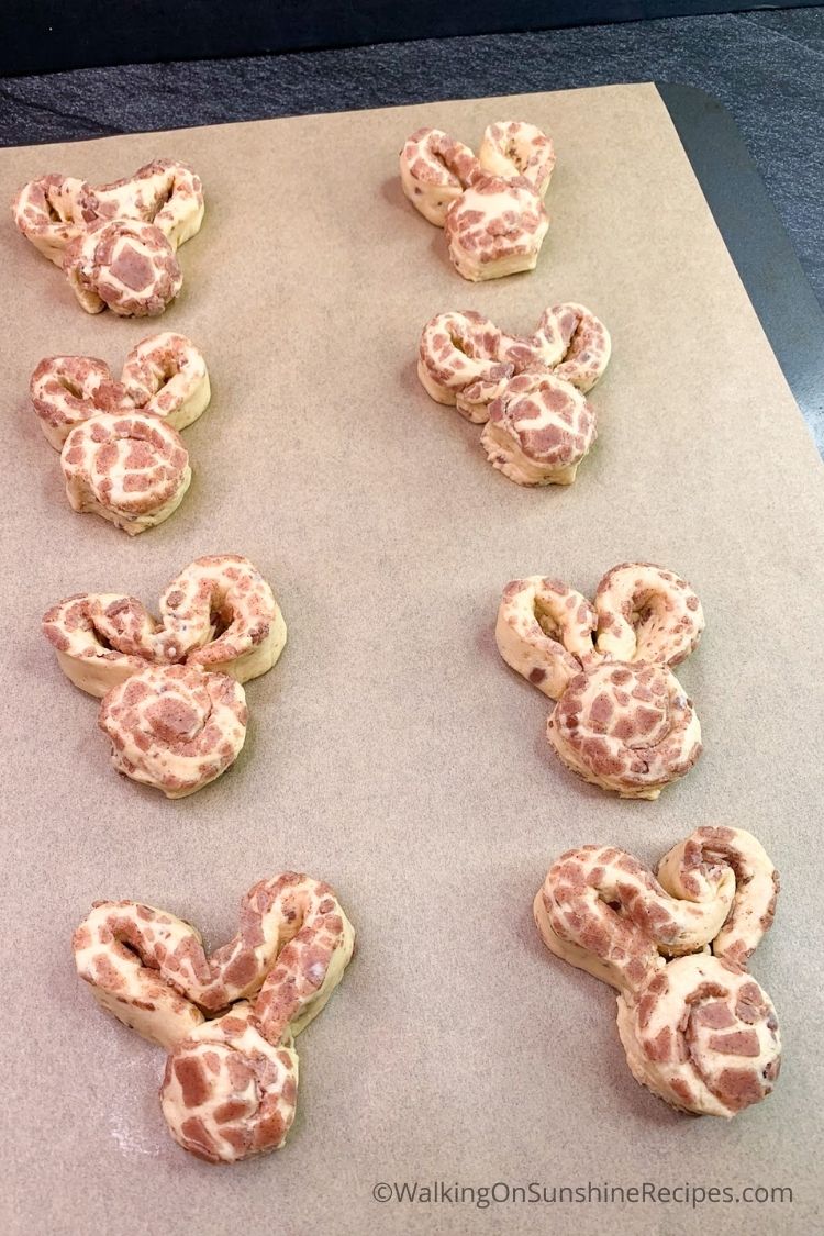 Pillsbury cinnamon rolls shaped into bunnies before baking on parchment lined baking tray. 