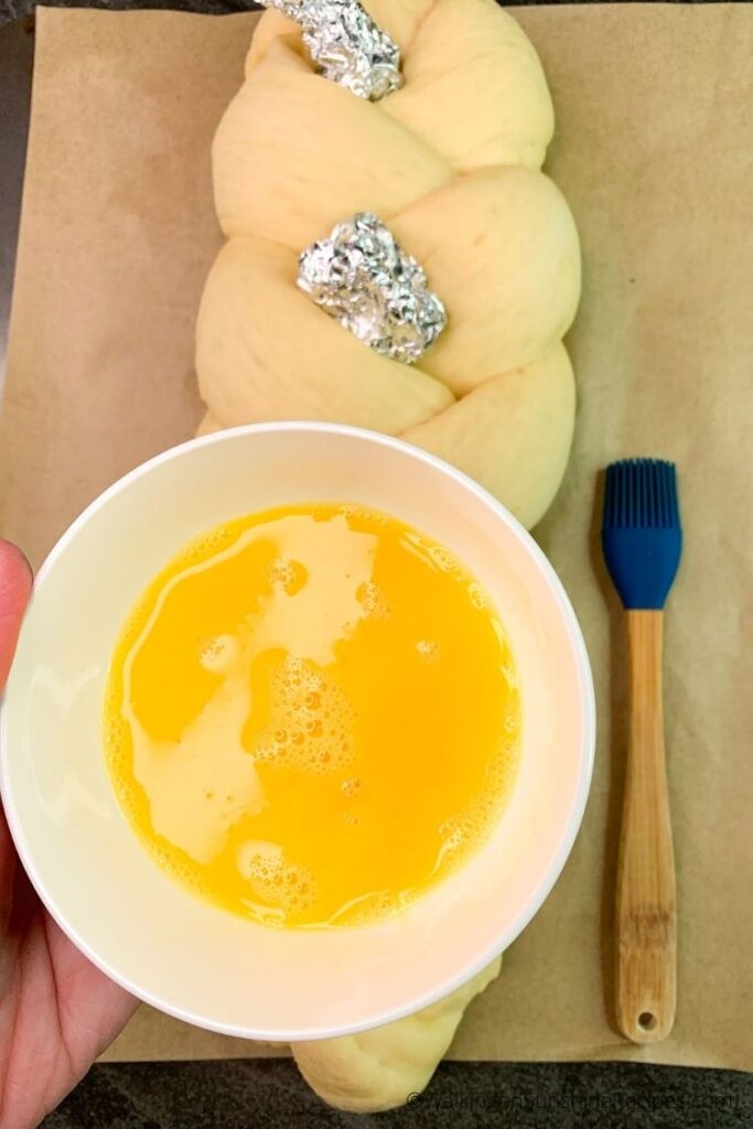 Brush egg wash on top of risen bread dough braid.
