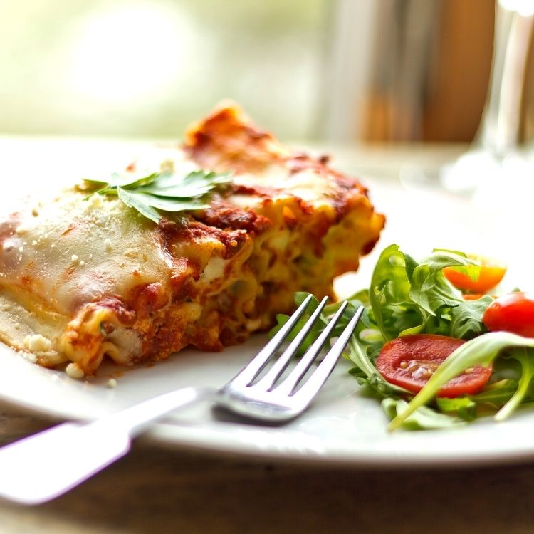 Lasagna on white plate with salad.