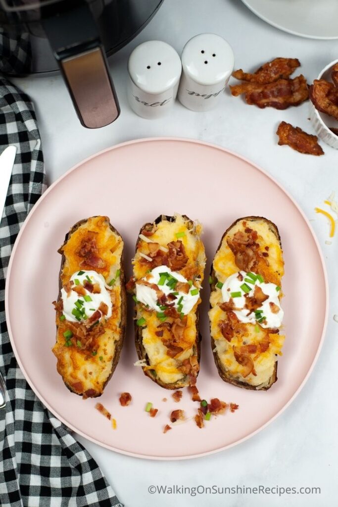 twice baked potatoes on pink plate with crumbled bacon. 