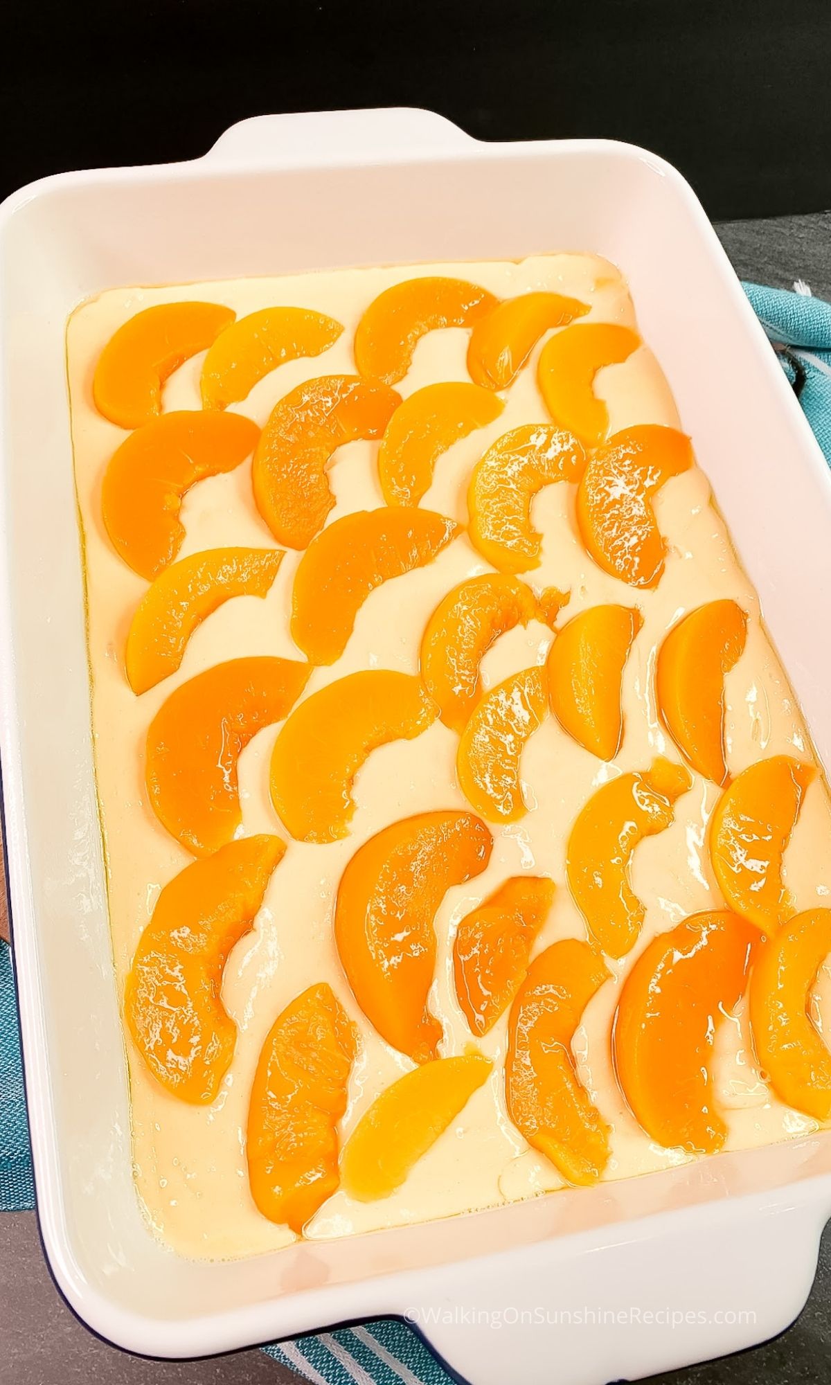 Sliced canned peaches on top of cake batter in baking dish. 