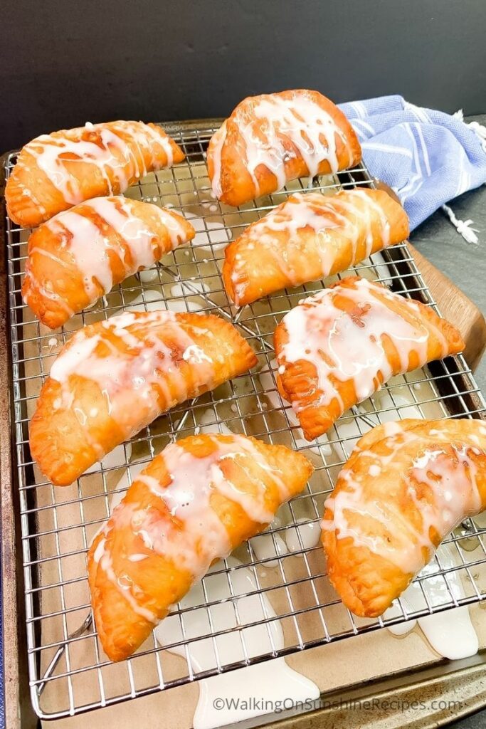 Fried Peach Pies using Canned Biscuits with powdered sugar glaze dripping on top of baking rack. 