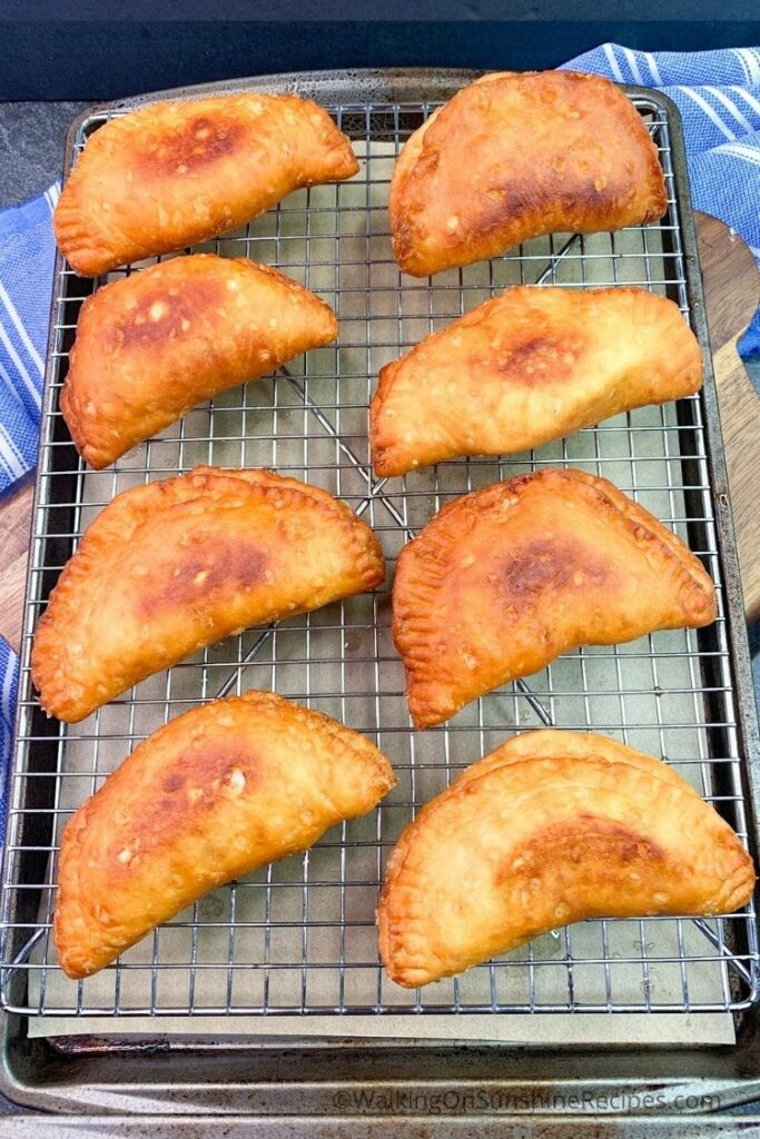 Golden brown fried peach pies cooling after frying. 